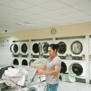 A woman folding clothes in a modern laundromat with various washing machines in the background.